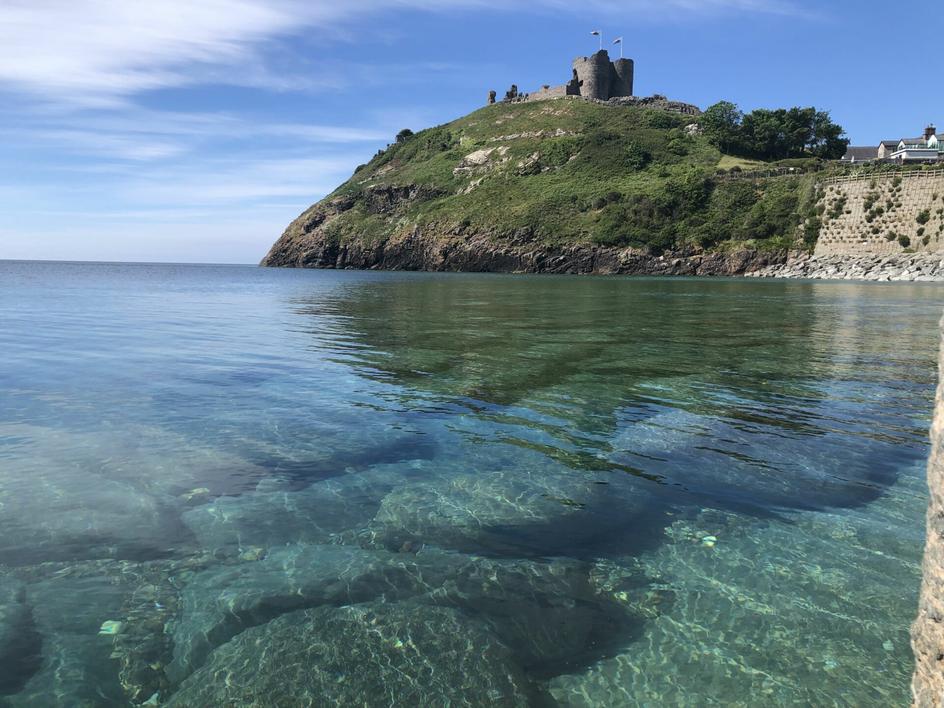 A castle on a hill with clear blue sea below. The sky is blue with some clouds.