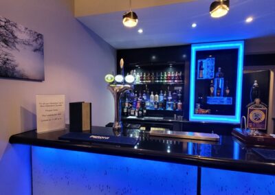 A contemporary hotel bar with a large selection of drinks. There is blue lighting and a bar stool.