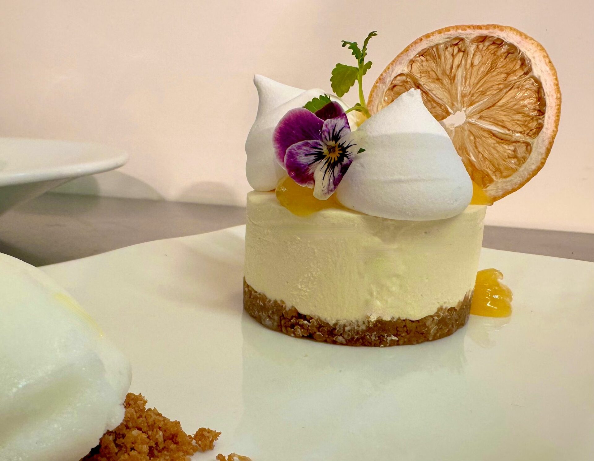 A beautiful cheesecake with meringue topping and orange slice topped with a pansy flower.